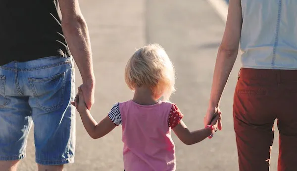 Un jeune enfant tenant la main de ses deux parents, vus de dos.
